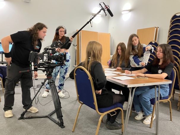Youth Acting for Screen (Film & TV) A group of people filming a scene at a table with cameras and sound equipment.