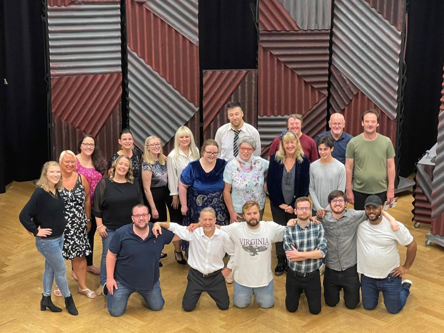 Group photo of diverse people posed together in a theatre space.