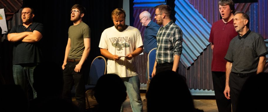 A group of six men standing on stage during a performance.