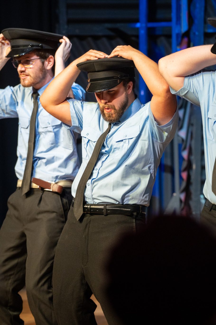 Three male performers dressed as police officers with hats, dancing on stage.