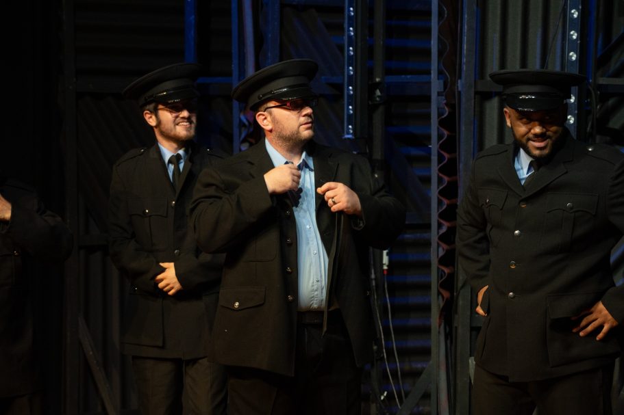 Four performers in police uniforms, smiling and adjusting their attire on stage.