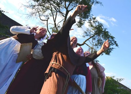 A group of people in historical costumes posing and gesturing joyfully outdoors.