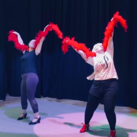 Burlesque Two performers in vibrant red feather boas pose energetically on stage.