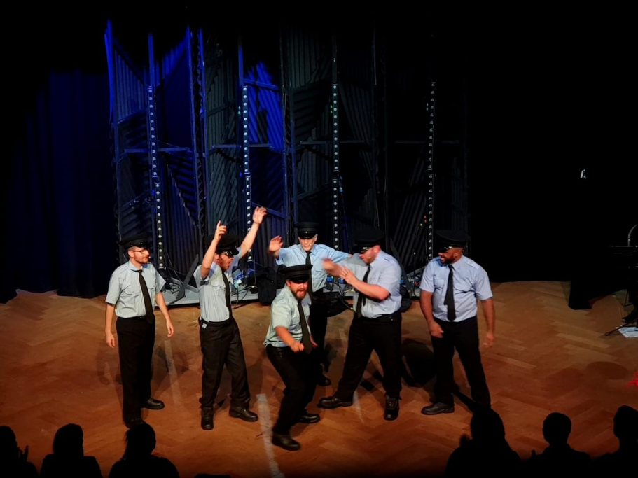 A group of six performers in shirts and ties, engaging in a dynamic stage performance.