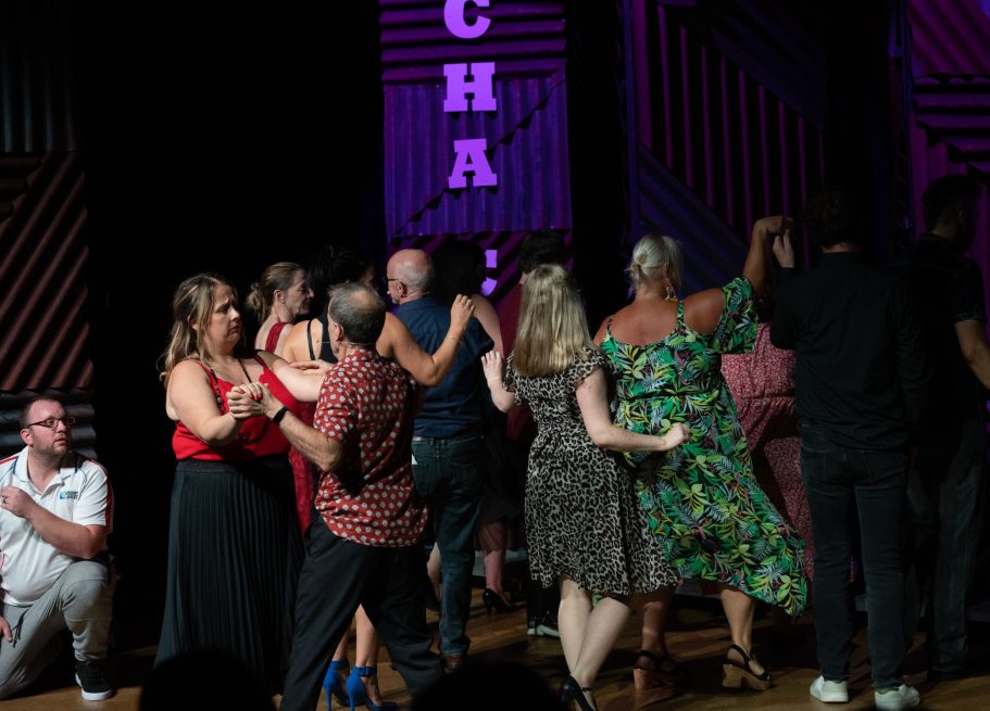 People dancing closely in a lively indoor setting with colourful lighting.
